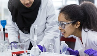 Students conducting a science experiment with lab glassware, white coats and eye protection