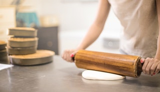 Person in white t-shirt rolling a pin in dough