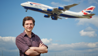 Paul Williams stands with arms crossed as plane takes off in background.
