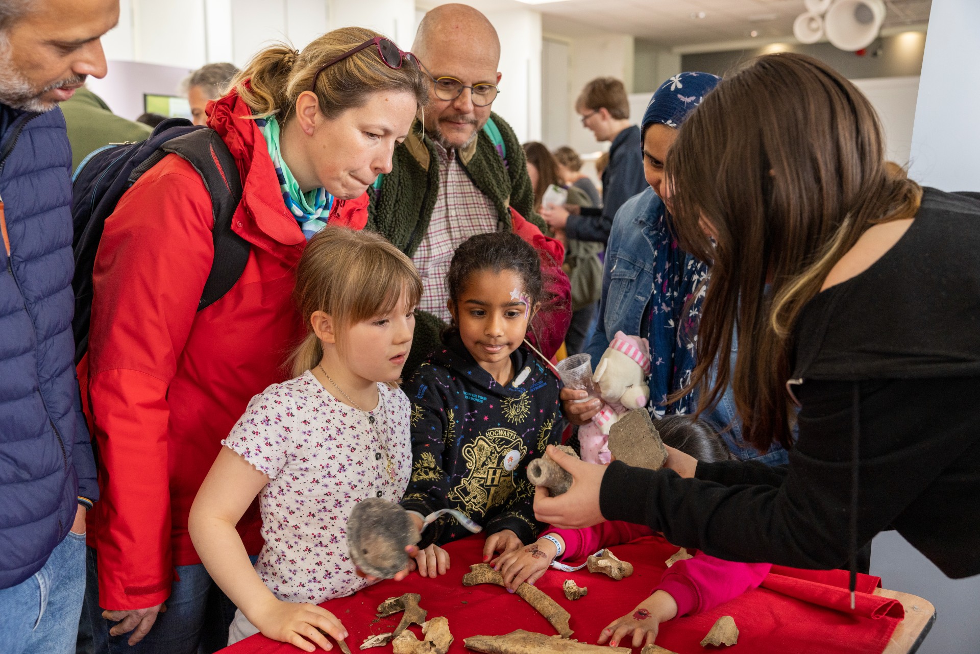 Two girls and some nearby adults are shown some ancient artefacts at an exhibit stand