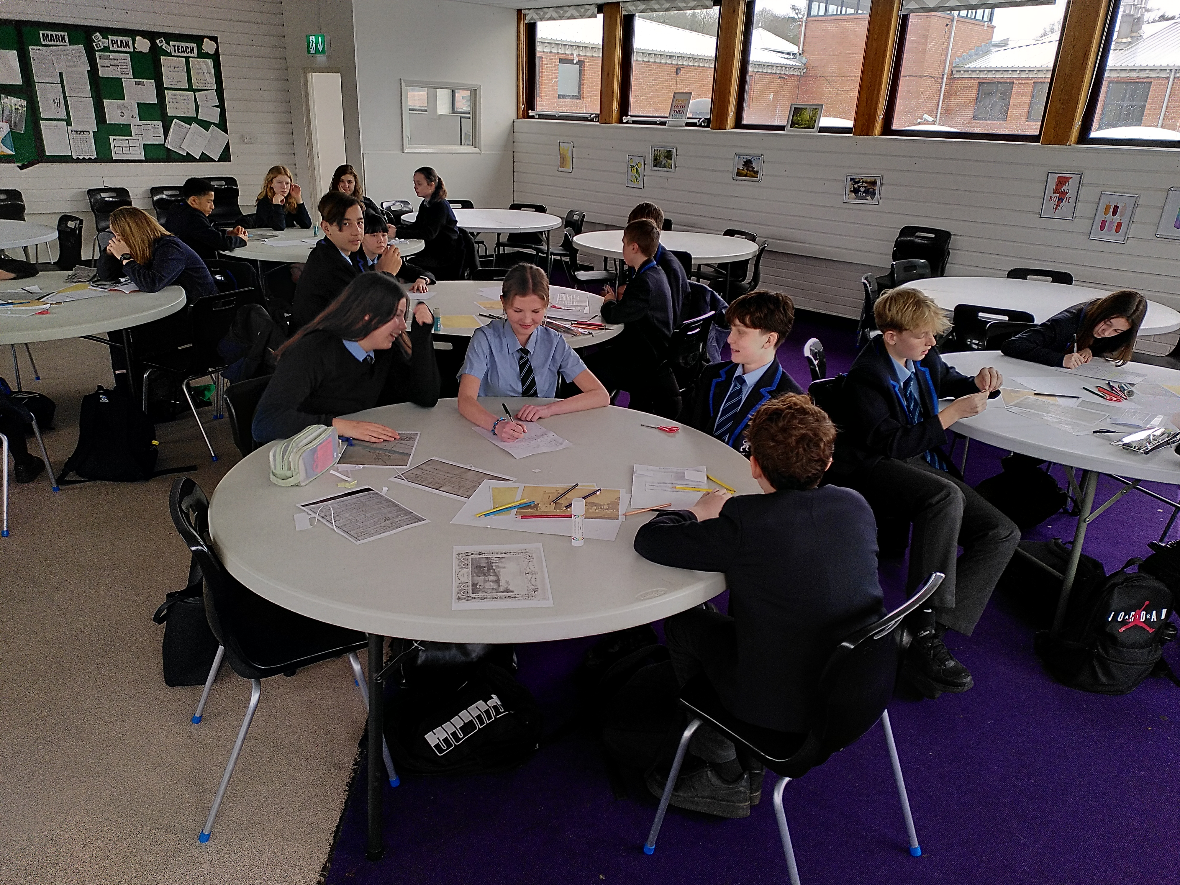 School children sit in groups around tables discussing a history project