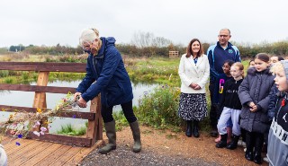 Professor Helen Bilton cuts a ribbon of wildflowers while a group of school children and school teachers look on