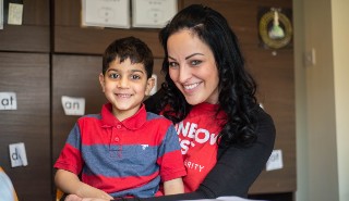 A young Asian boy sitting in the lap of a white woman who works for Rainbow Trust Children's Charity