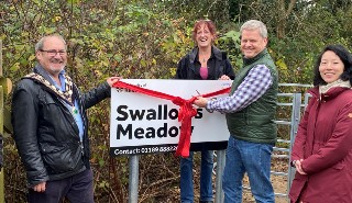 A white man cuts a ribbon placed in front of a sign, as part of an opening ceremony, surrounded by onlookers