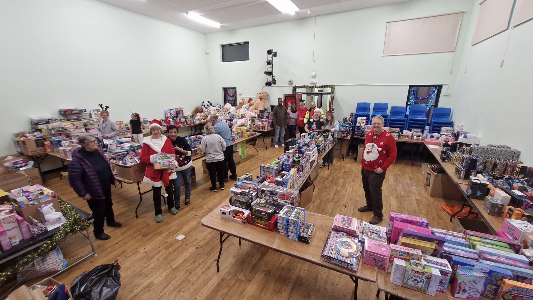 A hall with hundreds of toys and gifts stacked on tables, with some volunteers helping to sort them
