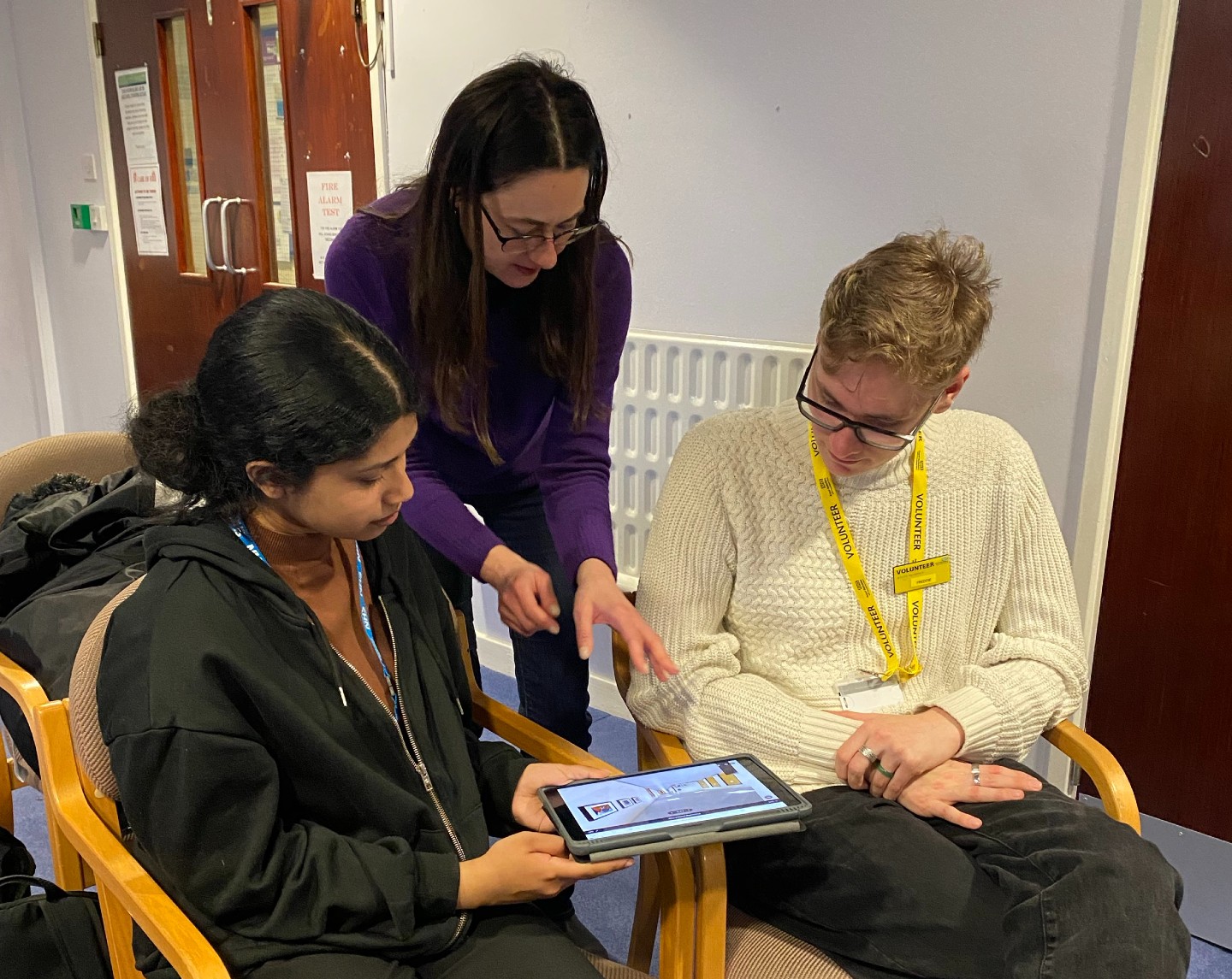A woman shows two teenagers a digital image of a hospital space on a tablet