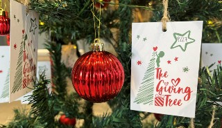 A close up of a red bauble and gift tag with the text "the giving tree" on a green Christmas tree