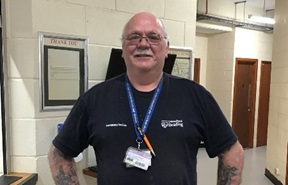 Trevor Kessell, standing in a corridor looking straight at the camera and smiling. 