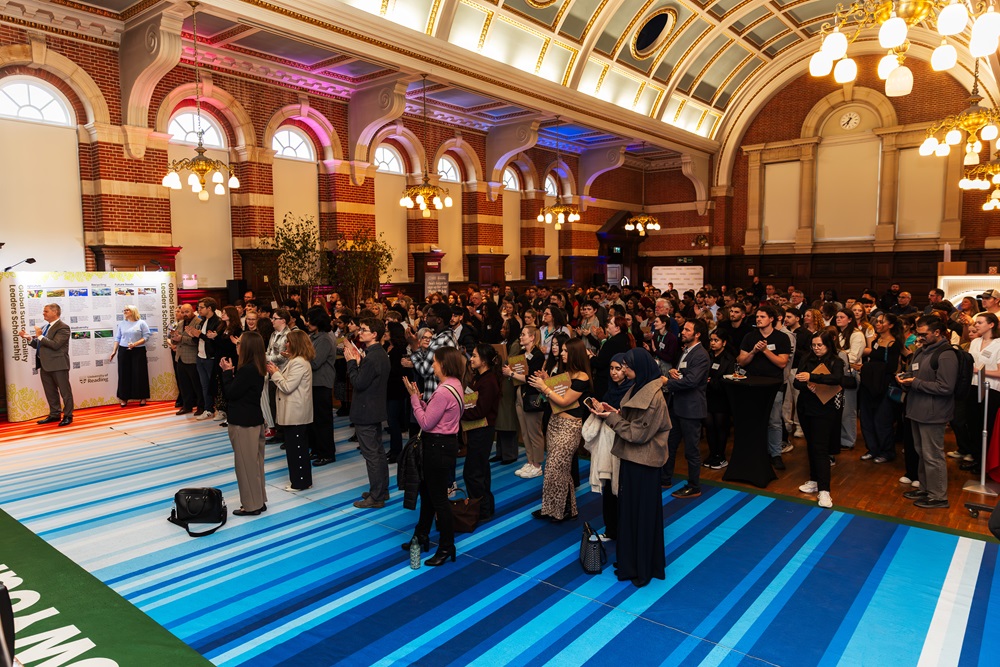 A large audience in the Great Hall, standing on a large climate stripes floor graphic