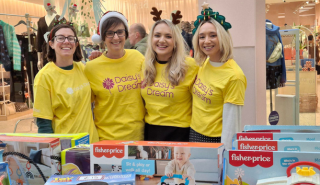 Four women in Daisy's Dream T shirts and Christmas hats volunteer at a stall selling toys for the charity