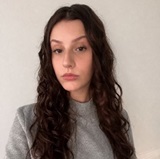A woman with long, dark hair wearing a grey jumper