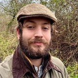 A man with a beard and wearing a flat cap and outdoor jacket