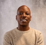 A man with a bald head wearing a beige jumper