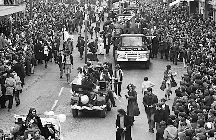 Black and white photo of vehicles parading down a road lined with crowds
