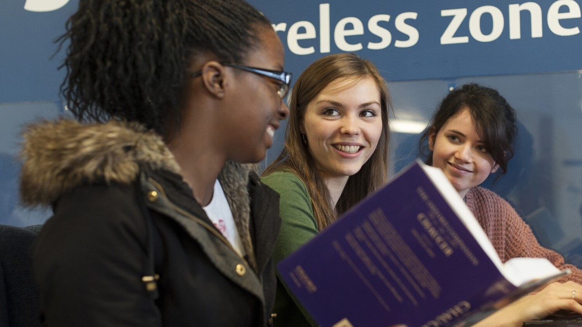 Three students laughing and looking at a book
