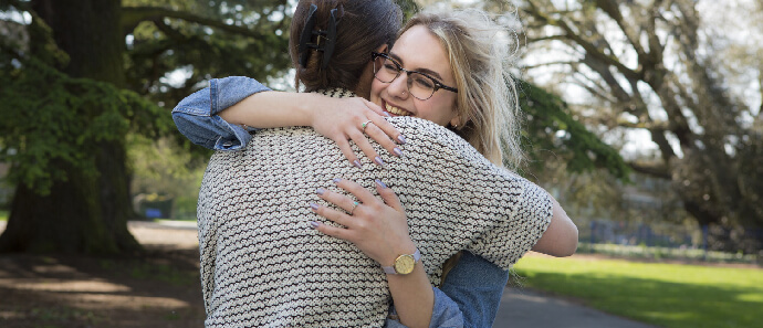 Two female friends share a hug outside.